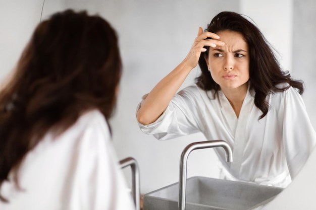 Mujer preocupada comprobando las arrugas en el espejo en el baño