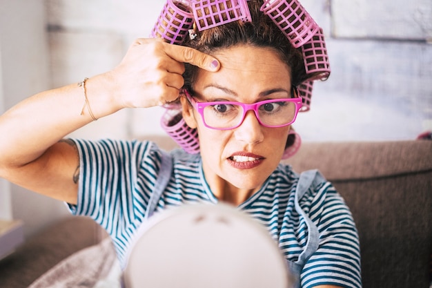 Mujer preocupada comprobar las arrugas de la piel y el párpado. Concepto de personas mujeres adultas de envejecimiento y anti edad. Rulos en el cabello. Señora bonita mirándose en el espejo en casa haciendo belleza