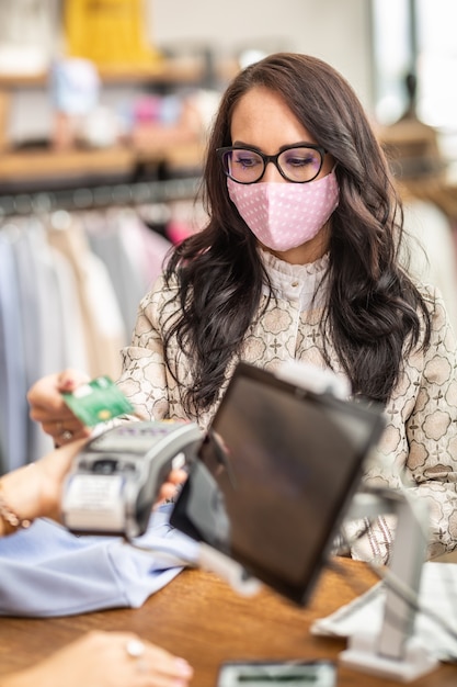 Una mujer preocupada por el coronavirus paga sin contacto con una tarjeta en la tienda con una mascarilla.