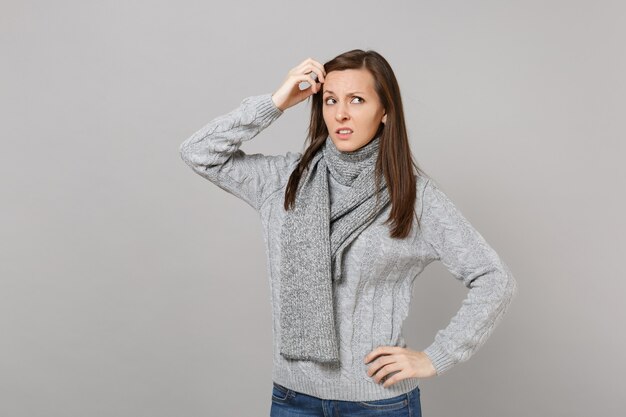 Mujer preocupada pensativa en bufanda de suéter gris mirando hacia arriba sosteniendo la mano cerca de la cabeza aislada sobre fondo gris. Estilo de vida de moda saludable, personas sinceras emociones concepto de estación fría. Simulacros de espacio de copia.