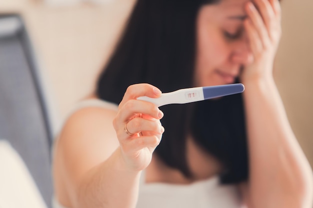 mujer preocupada con prueba de embarazo positiva en la cama