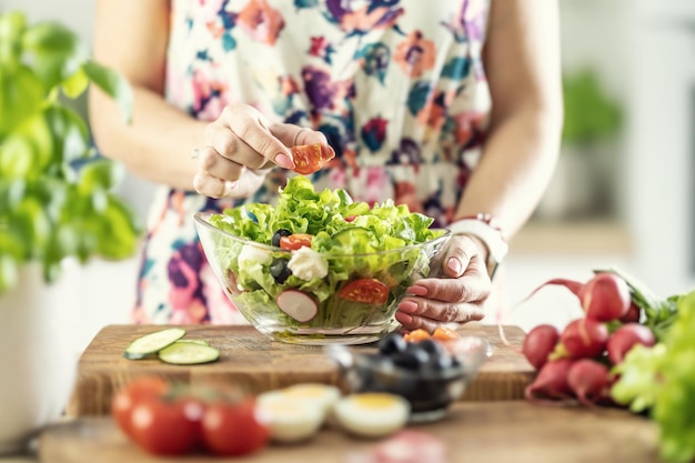Una mujer prepara una ensalada saludable y pone un tomate en rodajas en un bol
