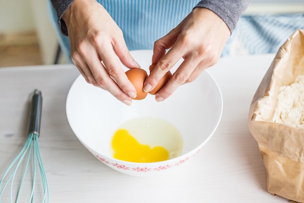 Foto una mujer prepara la masa para el pastel, rompe un huevo en una taza. ingredientes para hacer masa.