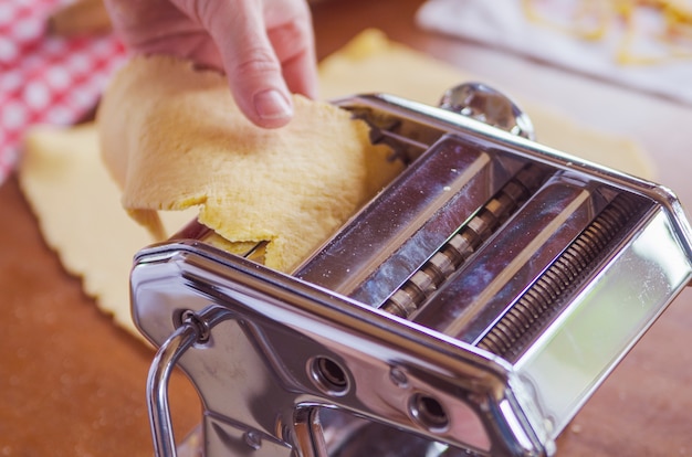 La mujer prepara las pasta italianas tradicionales de los tallarines en la máquina casera.