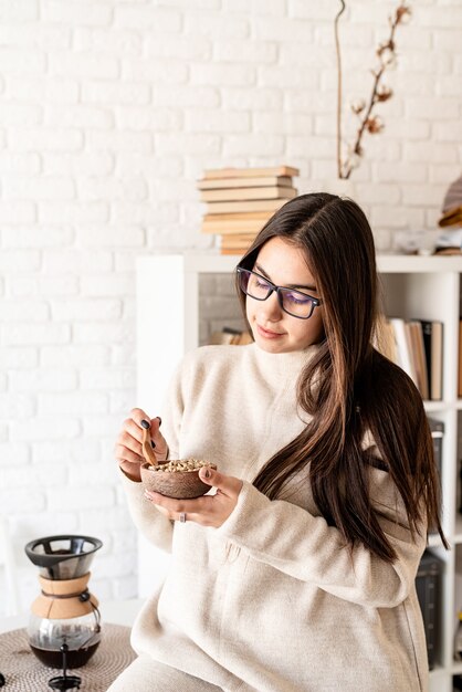 Mujer preparando café en una cafetera, oliendo granos de café verde