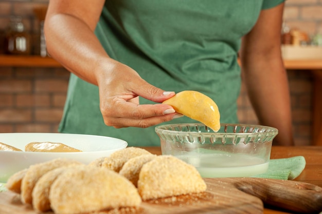 Mujer preparando croquetas rellenas de carne brasileña risolis de carne con leche y pan rallado en una mesa de madera