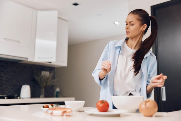 Una mujer preparando ensalada saludable en la cocina con verduras frescas y un cuenco de verduras mixtas