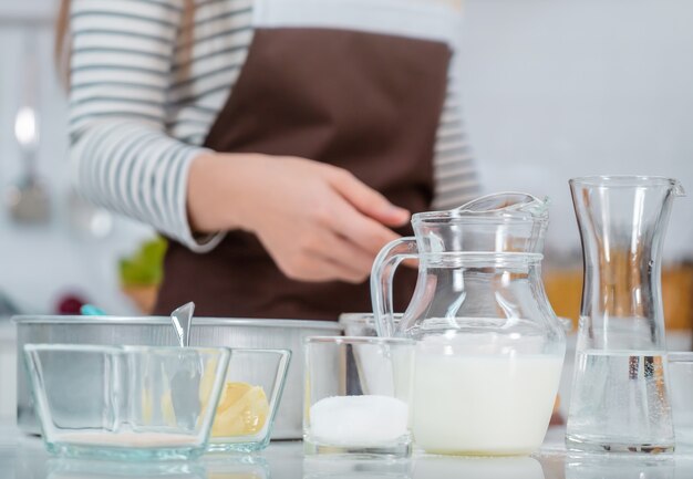 Foto la mujer está preparando los ingredientes de la panadería en la mesa de la cocina con leche, huevo, agua y harina.