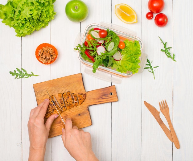 Mujer preparando una lonchera saludable con pechuga de pollo a la parrilla y verduras frescas