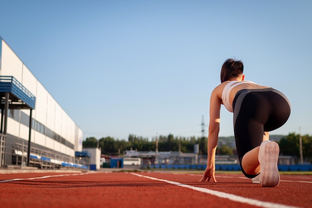 Mujer preparándose para comenzar en el estadio, entrenamiento de verano al aire libre. Mujer ejecutar entrenamiento al aire libre. Concepto de salud y deporte.