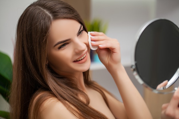 Mujer preparándose para el trabajo haciendo maquillaje por la mañana en el espejo del baño en casa