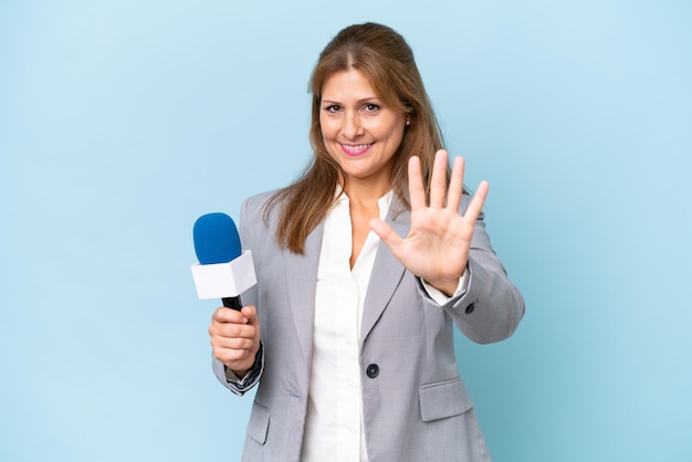 Mujer presentadora de televisión de mediana edad sobre fondo azul aislado contando cinco con los dedos