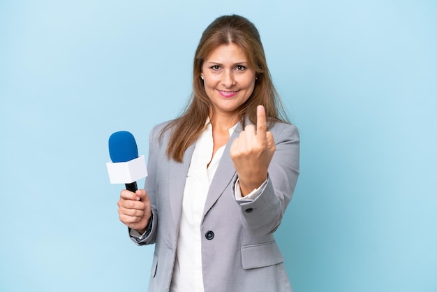 Mujer presentadora de televisión de mediana edad sobre fondo azul aislado haciendo el gesto de venir