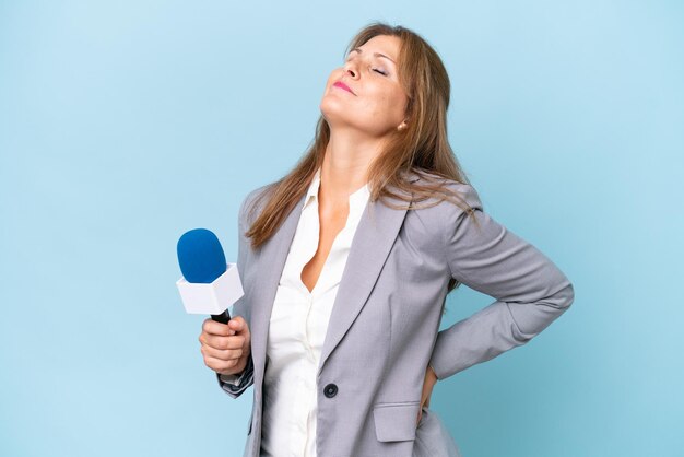 Mujer presentadora de televisión de mediana edad sobre un fondo azul aislado que sufre de dolor de espalda por haber hecho un esfuerzo