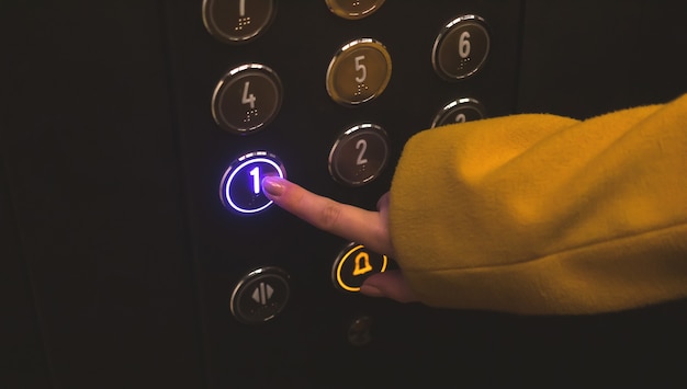 Mujer presione y presione el botón primer piso en el panel de control del ascensor vista de cerca de la mano