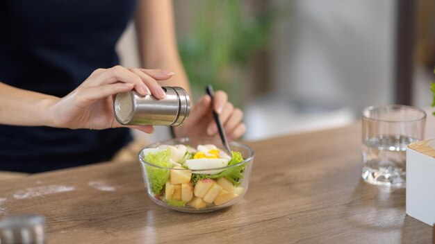 Mujer de primer plano agregando sal en su ensaladera saludable en la mesa de comedor de su casa Alimentos saludables y dietéticos