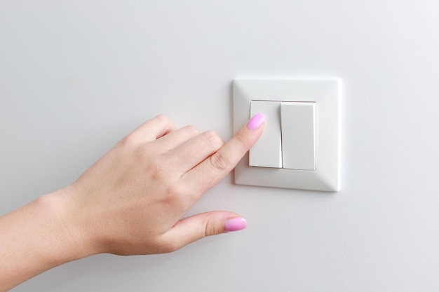 Mujer de primer plano enciende el interruptor en el interruptor de luz de casa de pared