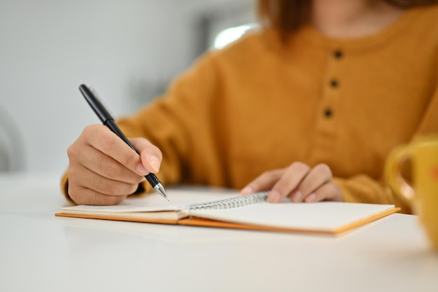 Mujer de primer plano escribiendo notas a mano en un planificador diario personal planificando la jornada laboral