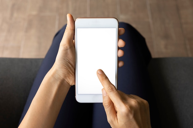 Mujer de primer plano de mano con pantalla blanca de teléfono inteligente en el sofá de la sala de estar. Concepto de tecnología, conexión, comunicación.