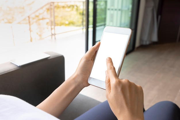 Mujer de primer plano de mano con pantalla blanca de teléfono inteligente en el sofá de la sala de estar. Concepto de tecnología, conexión, comunicación.