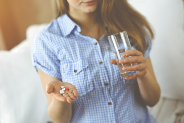 Mujer de primer plano sosteniendo pastillas para tomar medicamentos, curar el dolor de cabeza. Concepto de medicina durante el autoaislamiento y la pandemia de coronavirus