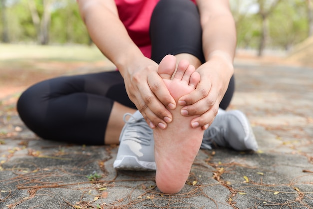 Mujer del primer que da masajes a su dolor del pie en el piso mientras que ejercita. La salud y el concepto de deporte.