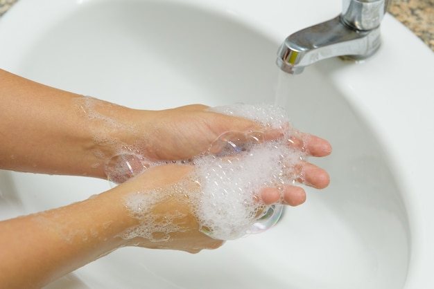 Mujer del primer que se lava las manos con el jabón debajo del faucet con agua en el cuarto de baño.