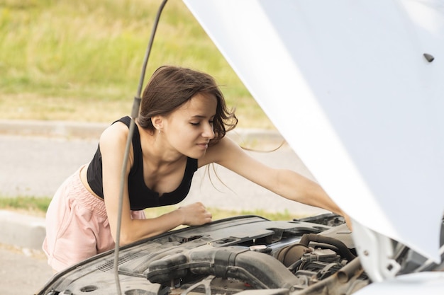 La mujer con problemas de motor con un auto roto en la carretera está molesta con un capó abierto esperando ayuda