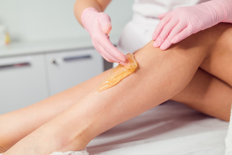 Mujer con procedimiento de depilación en las piernas con pasta de azúcar en el salón