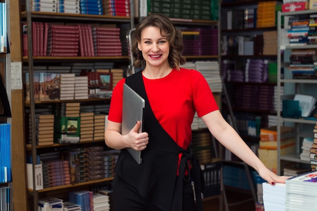 Foto mujer profesional educadora o gerente posando en la biblioteca pública de la escuela secundaria o la universidad sosteniendo una computadora portátil y sonriendo