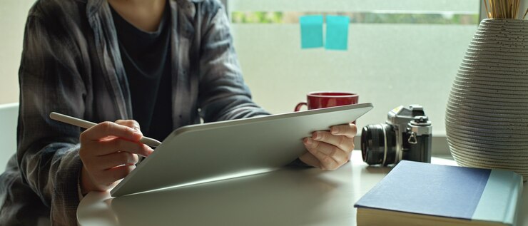 Foto mujer profesional independiente trabajando en tableta digital con lápiz óptico en la mesa de café junto a la ventana