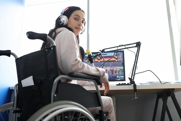 Mujer programadora independiente o streamer en auriculares modernos se sienta en silla de ruedas y usa