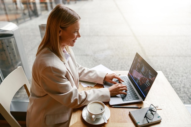 Mujer programadora independiente que trabaja en una computadora portátil mientras está sentada en un café con datos bien hechos