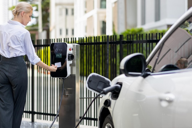 Foto mujer progresista paga por un punto de carga para alimentar un vehículo eléctrico recargable