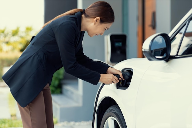 Mujer progresista recarga su coche EV en la estación de carga doméstica