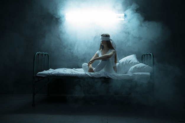 Mujer psicodélica con los ojos vendados sentada en la cama, cuarto oscuro .. Persona femenina psicodélica que tiene problemas todas las noches, depresión y estrés, tristeza, hospital psiquiátrico