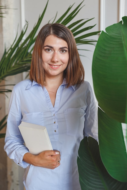 Mujer psicóloga con libro en oficina con plantas tropicales