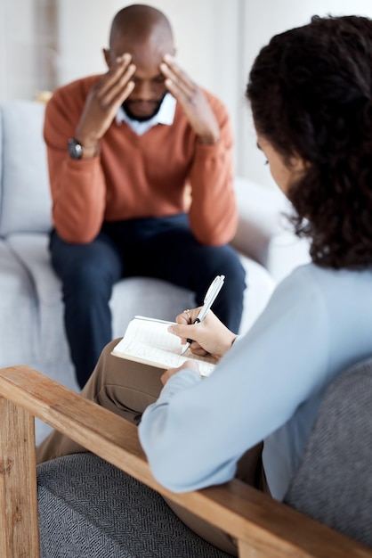 Foto mujer psicóloga que escribe a un hombre negro en terapia con dolor de cabeza por estrés de salud mental y depresión con ayuda informe médico de consulta sobre el diagnóstico del paciente problema de ansiedad y tristeza con depresión