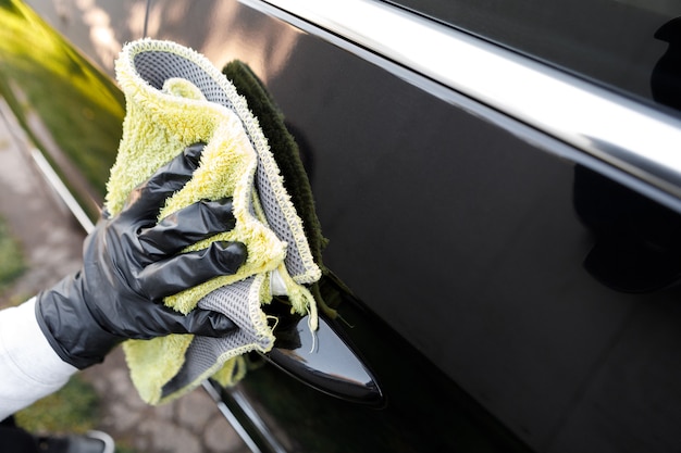 Foto mujer pule el coche utiliza un paño de microfibra y abrillantador para limpiar la carrocería del coche con esmalte