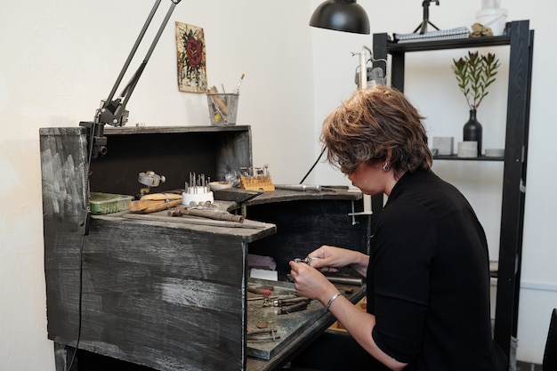 Mujer con pulidor abrasivo mientras trabaja en una nueva colección de joyas en un taller minimalista
