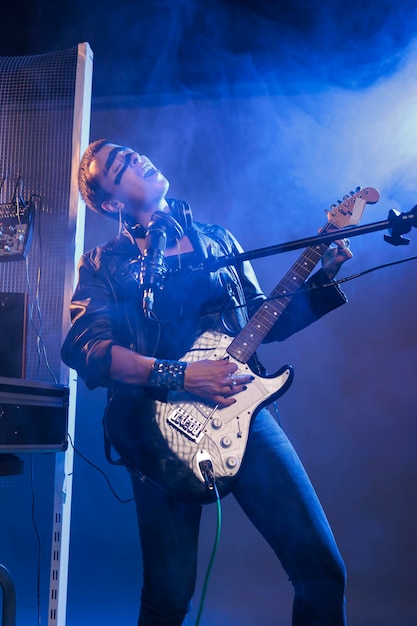 Mujer punk rockera cantando rock en guitarra con micrófono, haciendo presentaciones en vivo y sintiendo música heavy metal en el estudio. Interpretando una canción de rock alternativo y extasiado por el concierto en solitario.