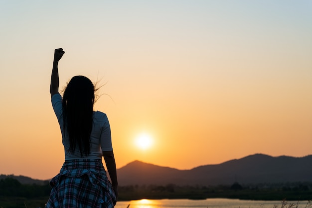 Mujer con el puño en el aire durante el atardecer, sentirse motivado, concepto de libertad.