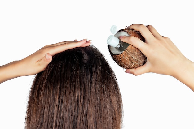 Mujer que aplica la botella y la tapa del aceite de coco al pelo en una mano en la vista posterior del aislante blanco.