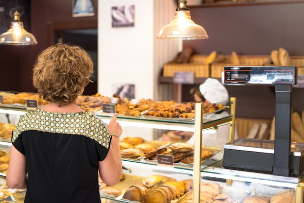 Mujer que apunta con un dedo a una bola de masa que quiere comprar en una panadería.