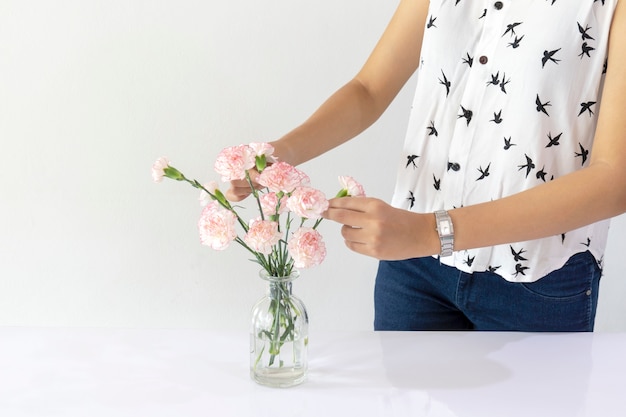 Mujer que arregla las flores del clavel en un florero de cristal en casa.