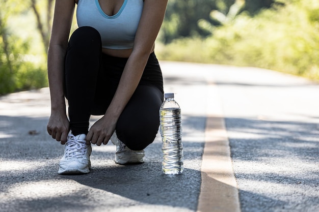 Una mujer que se ata los zapatos antes de trotar, está corriendo en un parque donde mucha gente viene a trotar por la mañana y por la noche, correr es una actividad popular. Concepto de salud con jogging.