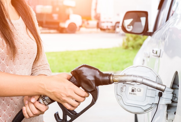 Mujer que bombea el combustible de la gasolina en coche en la gasolinera.