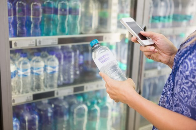 Mujer que compara el precio de una botella de agua con su teléfono