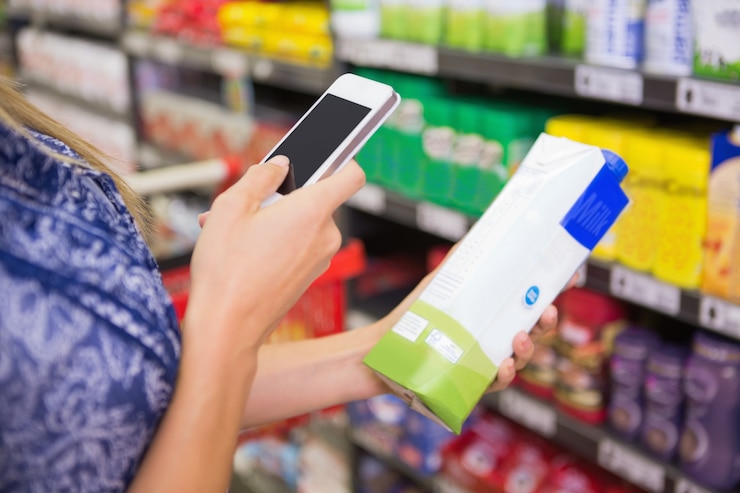 Foto mujer que compara el precio de un cartón de leche con su teléfono