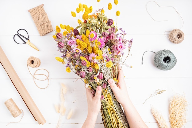 Mujer que compone el ramo de flores secas y hierbas, decoración de interiores de moda, idea de tienda de floristería artesanal. Vista superior, endecha plana